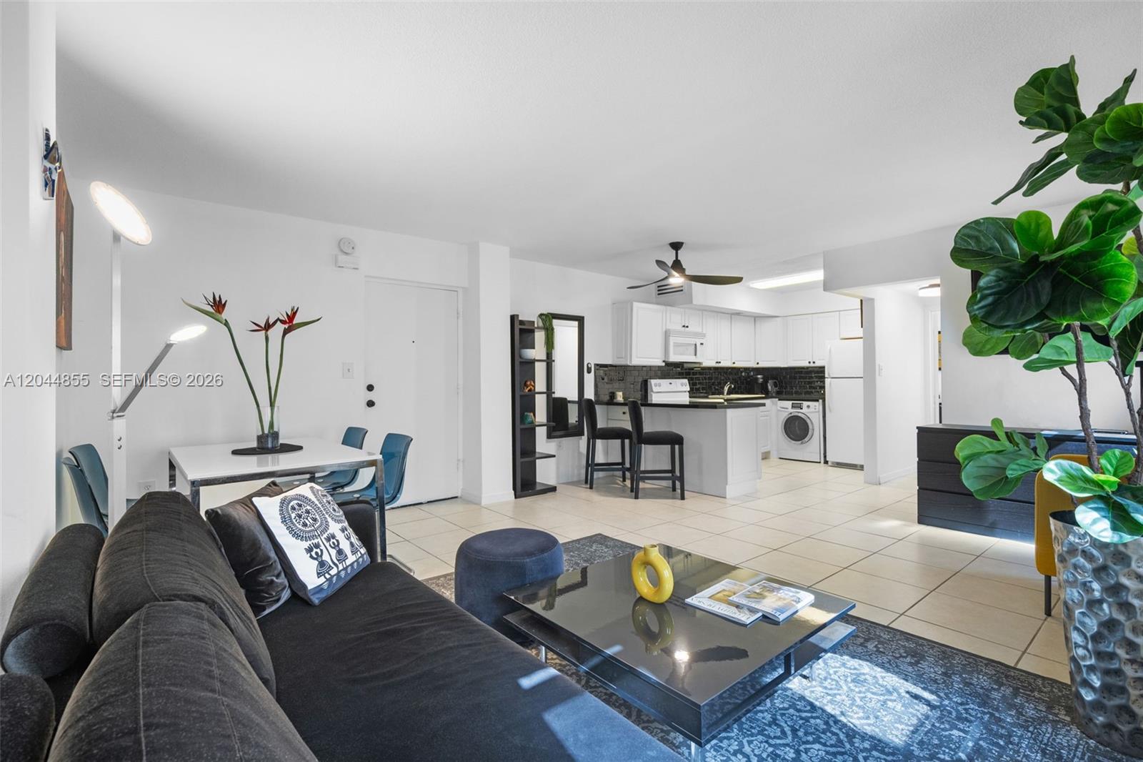 A living room with a black sofa and coffee table opens to a white kitchen — 801 S Ocean Dr # 207, Hollywood FL 33019, HOLLYWOOD, FL