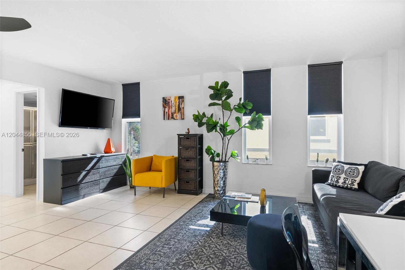 A living room features white walls, tile flooring, a black sofa, and a yellow armchair — 801 S Ocean Dr # 207, Hollywood FL 33019, HOLLYWOOD, FL