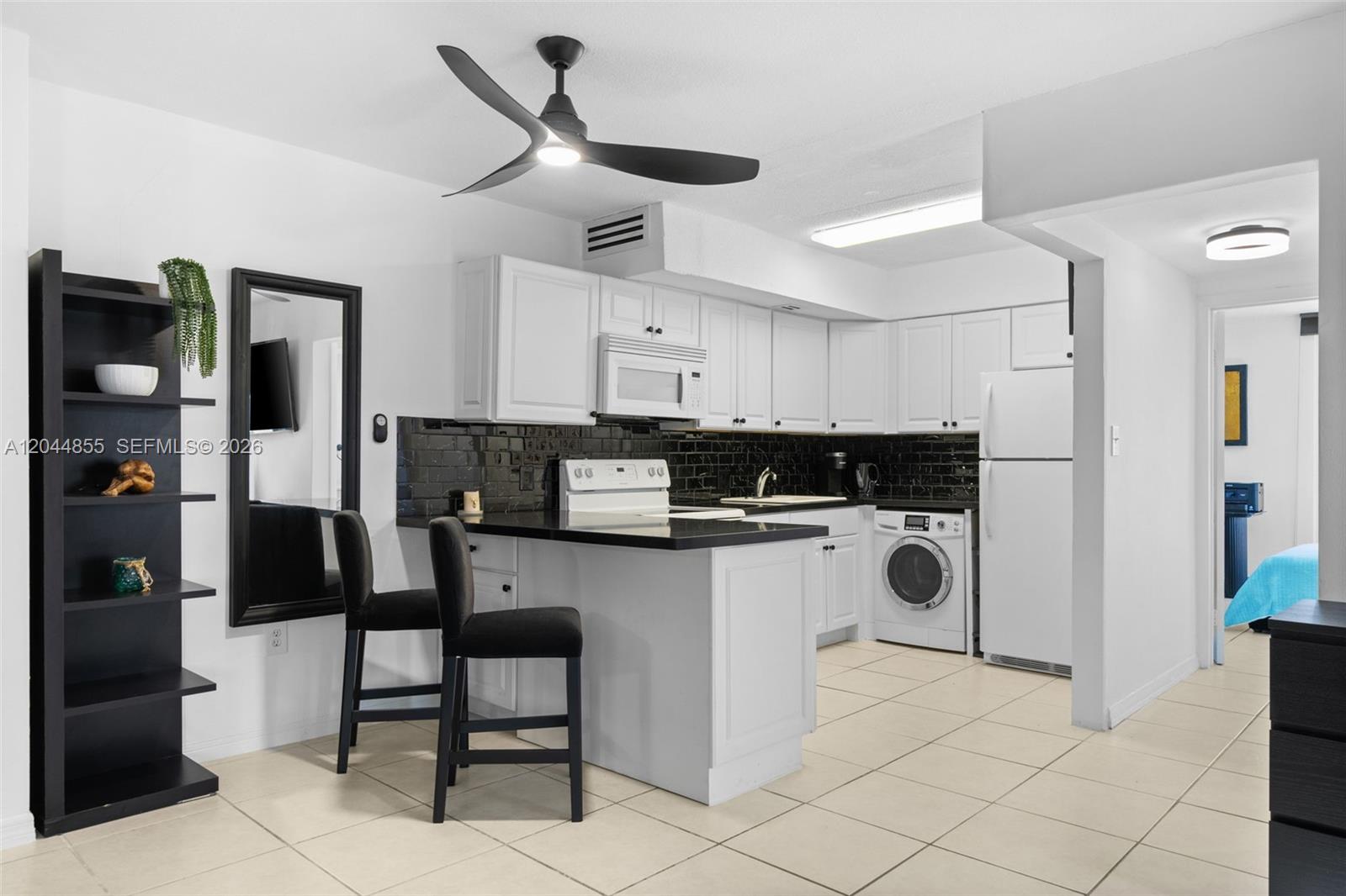 A kitchen features white cabinets, black countertops, a subway tile backsplash, and a laundry unit — 801 S Ocean Dr # 207, Hollywood FL 33019, HOLLYWOOD, FL