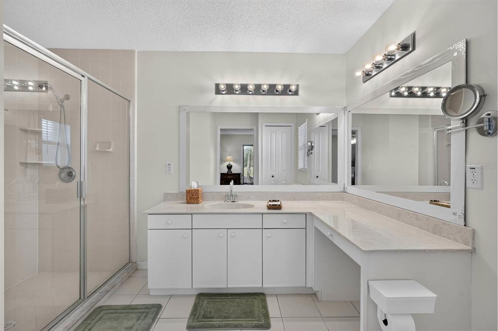 A bathroom features a white vanity with a stone countertop, dual mirrors, and a shower — 40 FLAMINGO DRIVE, PALM COAST, FL