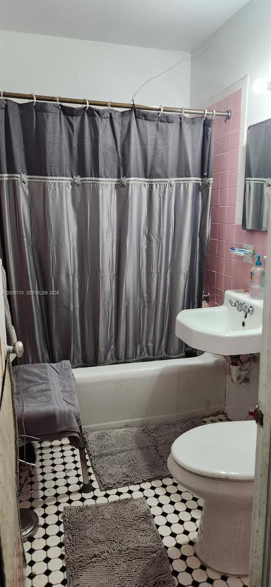 A bathroom features a pink tiled shower wall, a pedestal sink, and black-and-white floor tiles — 890 E 52nd St, Hialeah FL 33013, HIALEAH, FL