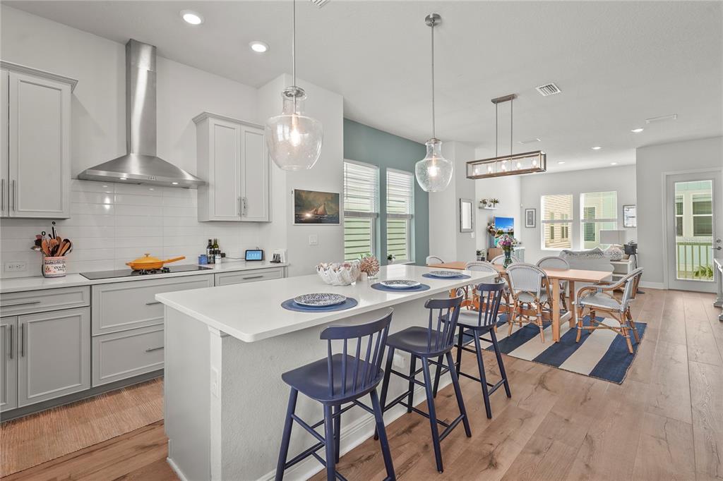 A modern kitchen features light gray cabinets, a white island with blue stools, and wood flooring — 2505 BOONE COURT, SARASOTA, FL