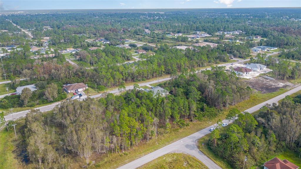 An aerial view shows a residential area with scattered houses, paved roads, and dense trees — 609-611 LADD STREET, LEHIGH ACRES, FL