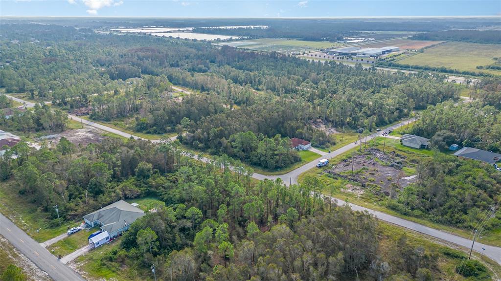 An aerial view shows a residential area with scattered houses, paved roads, and dense vegetation — 609-611 LADD STREET, LEHIGH ACRES, FL