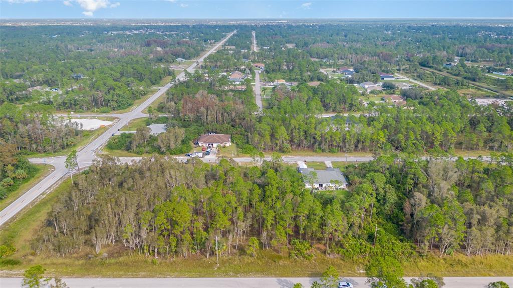 An aerial view shows a residential street with scattered houses surrounded by dense pine forests — 609-611 LADD STREET, LEHIGH ACRES, FL
