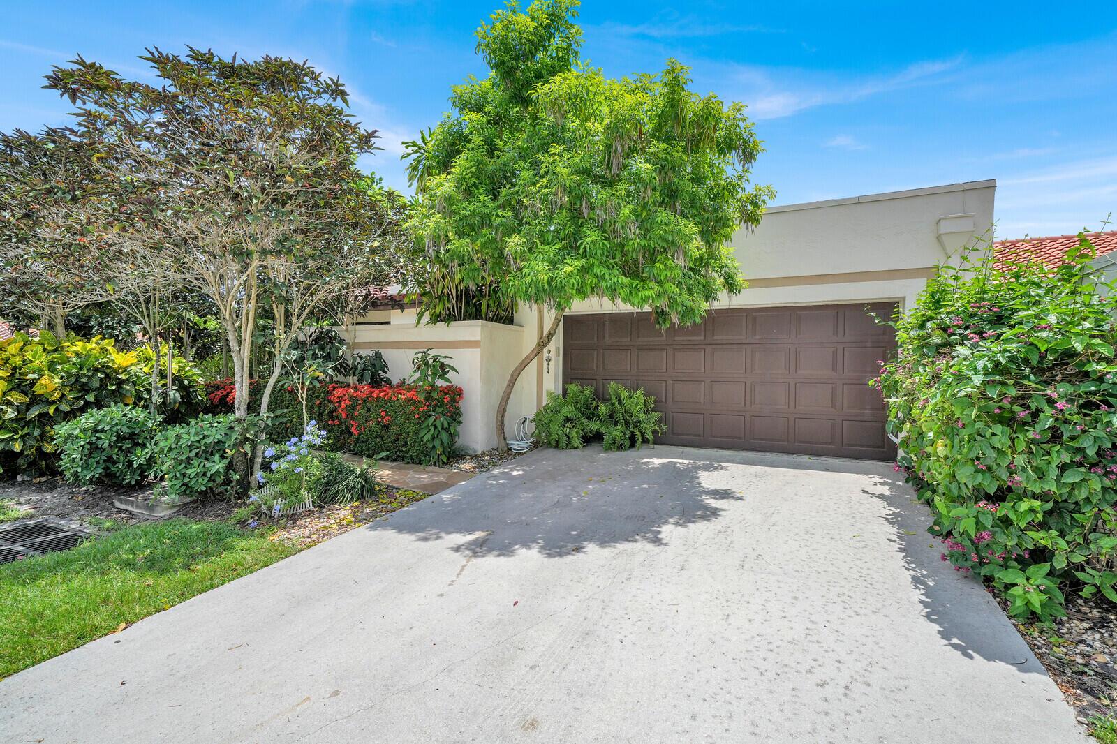 A concrete driveway leads to a brown garage door beside a house with lush landscaping — 21381 Sonesta Way, Boca Raton FL 33433, BOCA RATON, FL