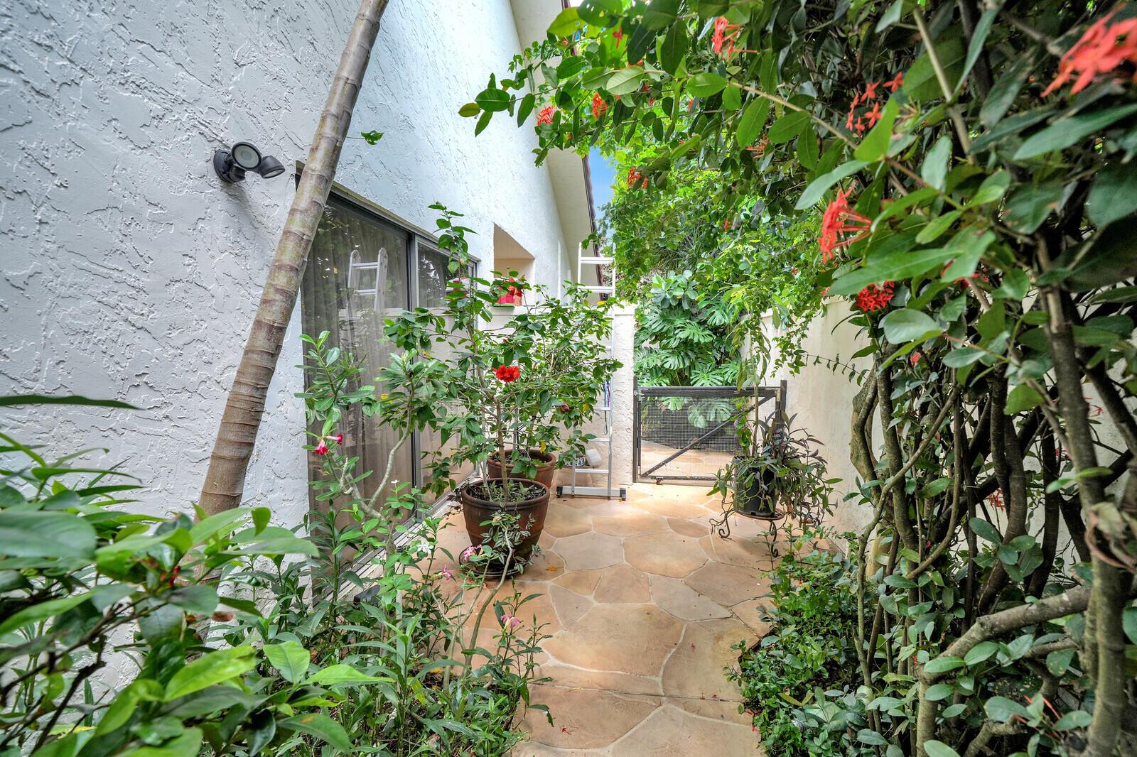 A stone-paved side patio features potted plants, a sliding glass door, and a metal gate — 21381 Sonesta Way, Boca Raton FL 33433, BOCA RATON, FL