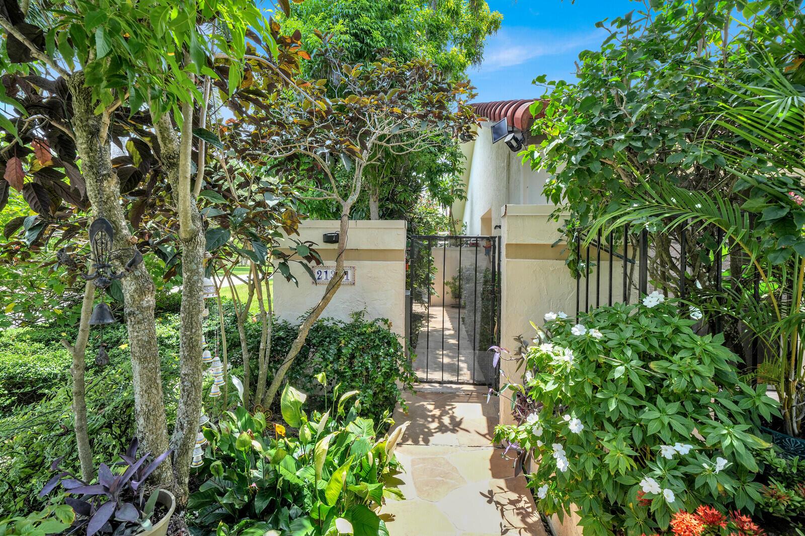 A stone walkway leads through a lush garden to a gated entrance of a house — 21381 Sonesta Way, Boca Raton FL 33433, BOCA RATON, FL