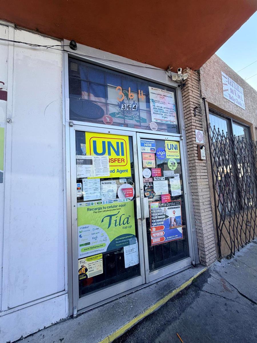 The exterior of a storefront features a glass door covered in various business service advertisements — 364 W Avenue A, Belle Glade FL 33430, BELLE GLADE, FL