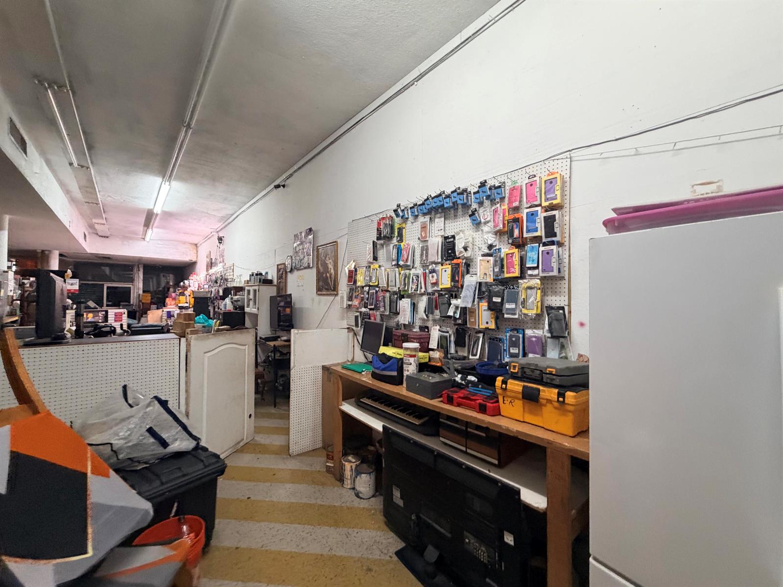 A cluttered commercial workshop features a pegboard wall displaying various phone accessories and tools — 364 W Avenue A, Belle Glade FL 33430, BELLE GLADE, FL