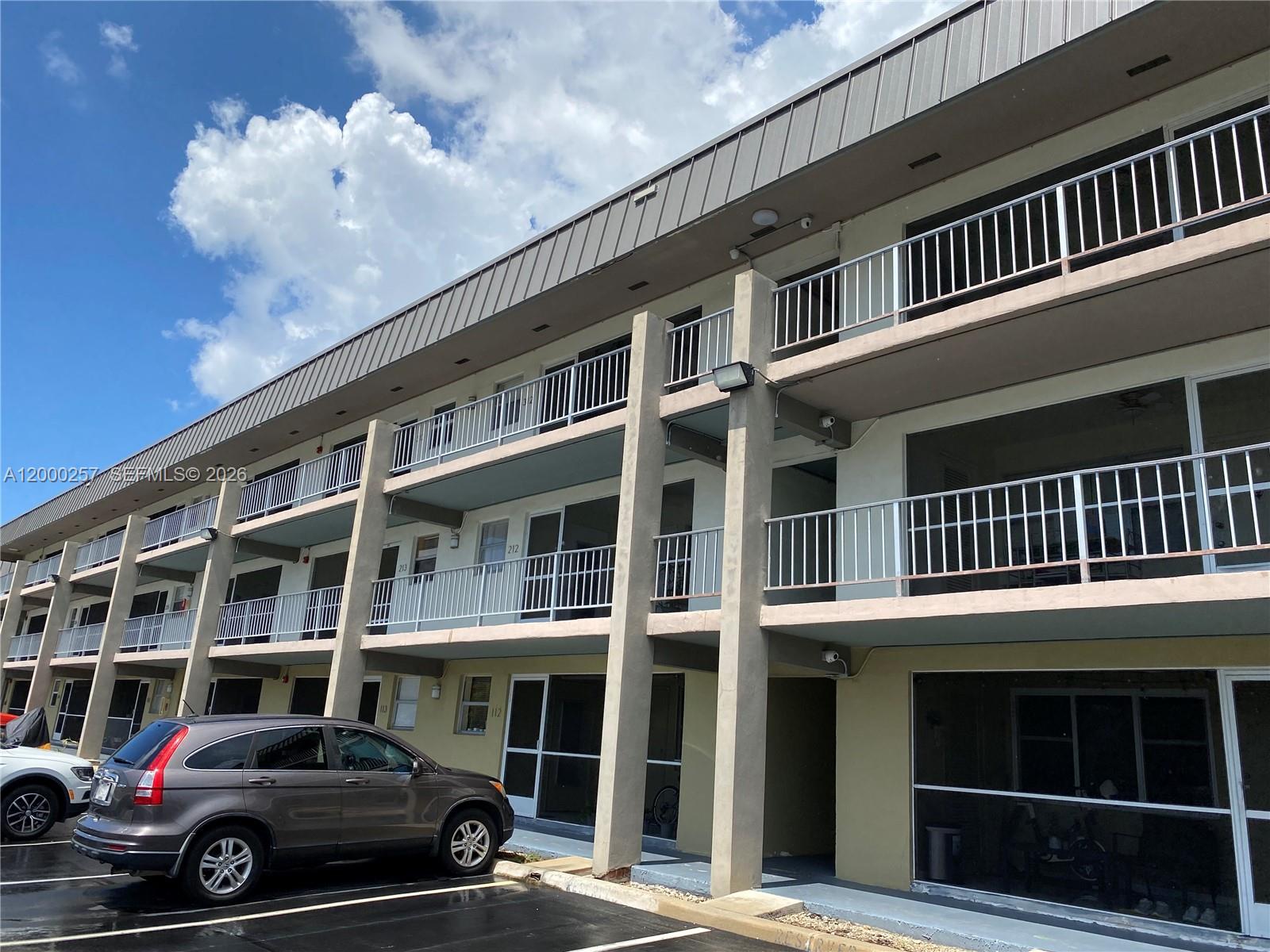 A kitchen features wood cabinets, white appliances, a glass-top stove, and tile flooring — 250 Layne Blvd # 110, Hallandale Beach FL 33009, HALLANDALE BEACH, FL