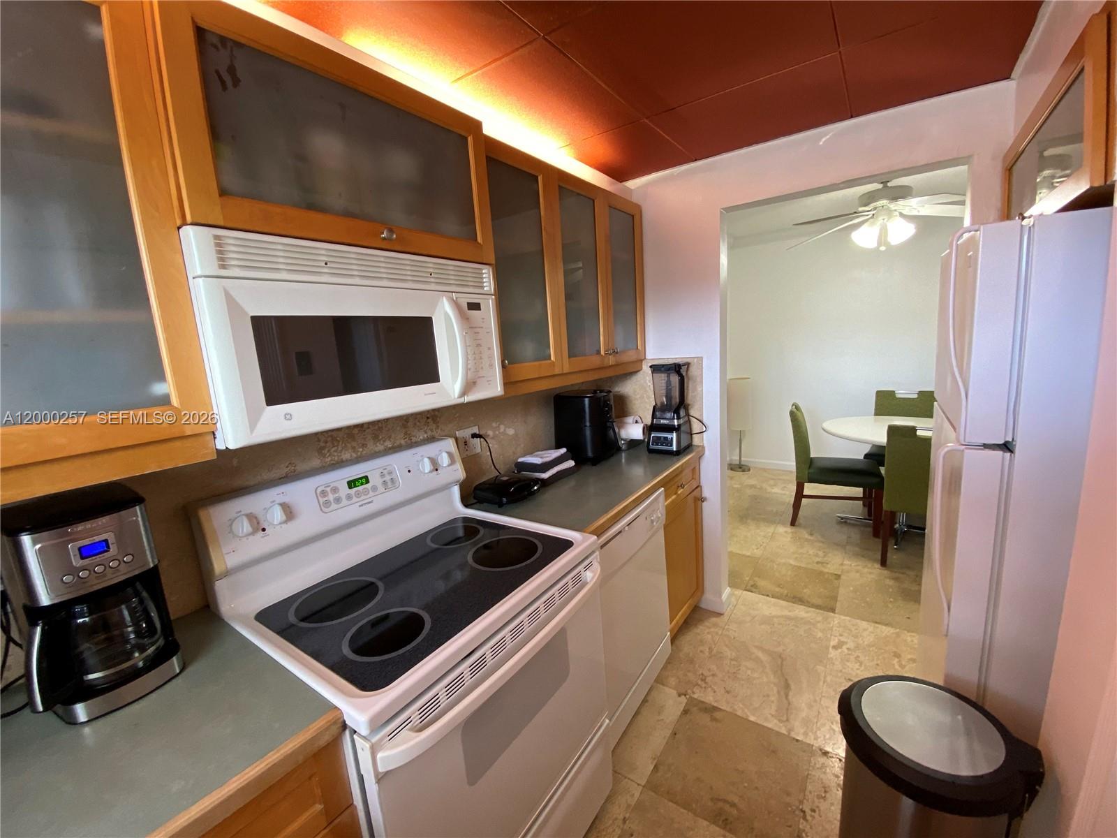 A view from a dining area looking into a galley kitchen with light wood cabinets — 250 Layne Blvd # 110, Hallandale Beach FL 33009, HALLANDALE BEACH, FL