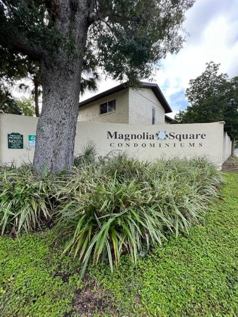 A large tree stands in front of a beige wall sign for Magnolia Square Condominiums — 501 EAST BAY DRIVE UNIT 104, LARGO, FL