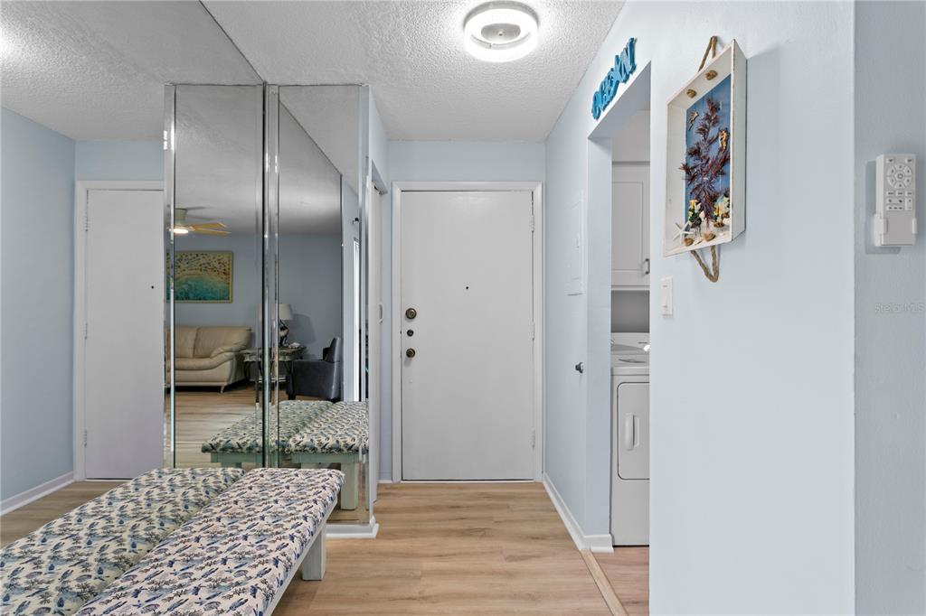 An entryway features light wood flooring, mirrored closet doors, a patterned bench, and a white door — 501 EAST BAY DRIVE UNIT 104, LARGO, FL