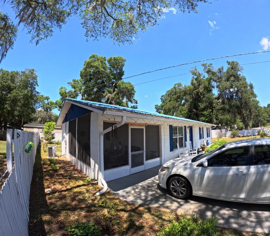 A white house with a blue roof and a screened-in front porch sits beside a car — 440 SW 264TH STREET, NEWBERRY, FL