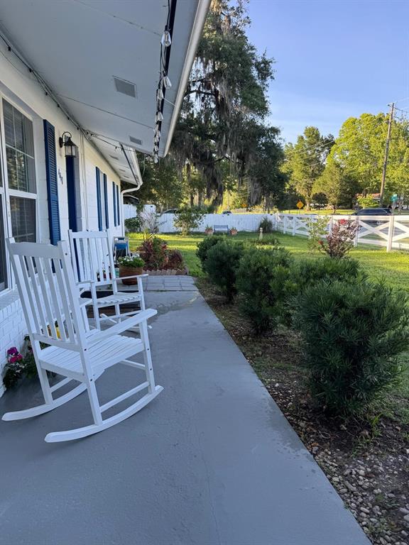A white house features a covered porch with two rocking chairs and a grassy yard — 440 SW 264TH STREET, NEWBERRY, FL