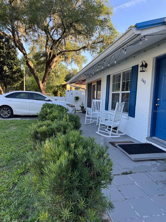 A white brick house exterior features blue shutters, a front porch with rocking chairs, and landscaping — 440 SW 264TH STREET, NEWBERRY, FL