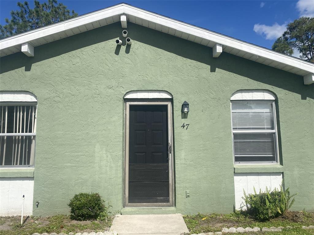 The exterior of a green house features a black front door and two windows — 47 W LAS PALMAS WAY, KISSIMMEE, FL