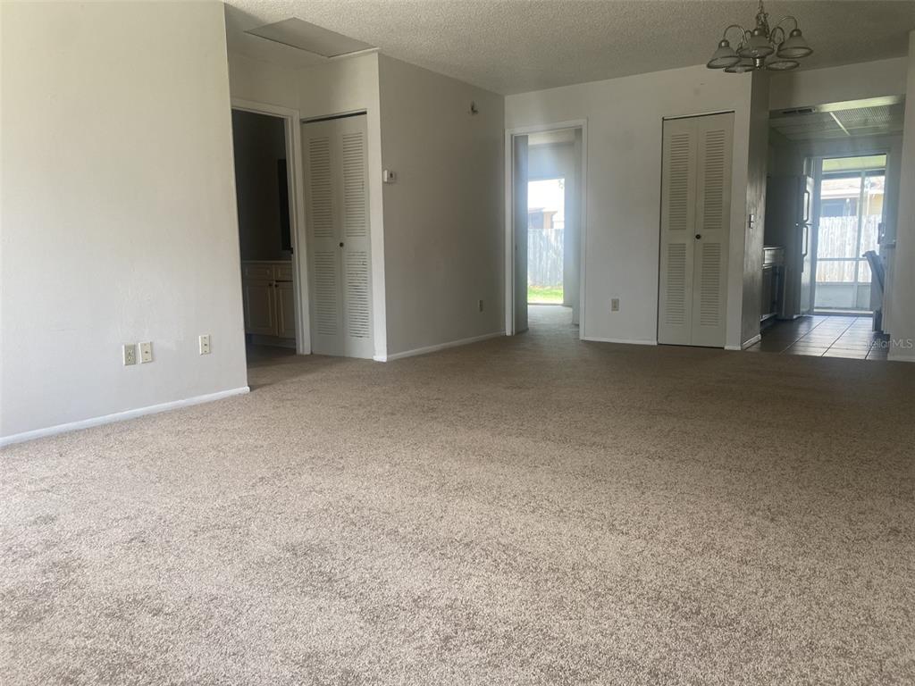 A carpeted living room features white walls, two sets of louvered closet doors, and a kitchen — 47 W LAS PALMAS WAY, KISSIMMEE, FL