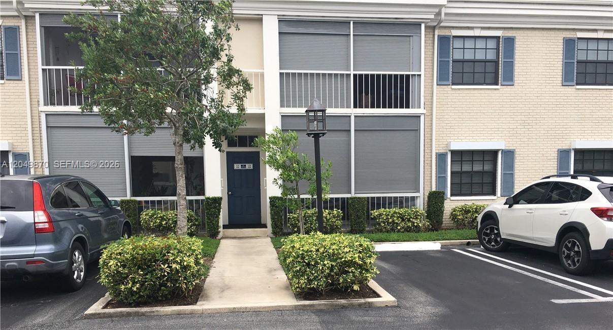 A two-story townhouse exterior features a blue front door, gray shutters, and two parked cars — 110 Cypress Club Dr # 108, Pompano Beach FL 33060, POMPANO BEACH, FL