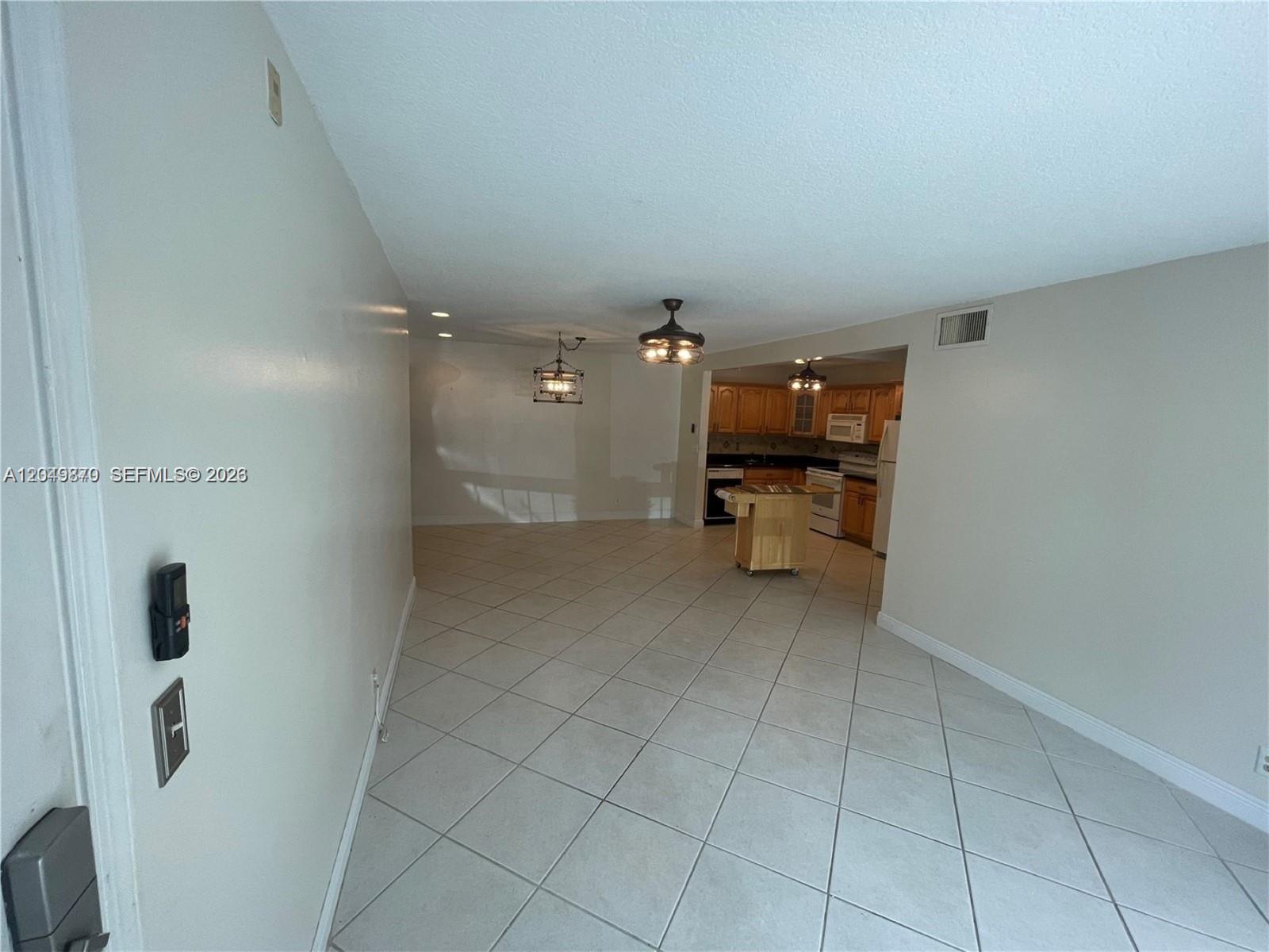 An open-concept living and dining area features light-colored tile flooring and a kitchen with wood cabinets — 110 Cypress Club Dr # 108, Pompano Beach FL 33060, POMPANO BEACH, FL