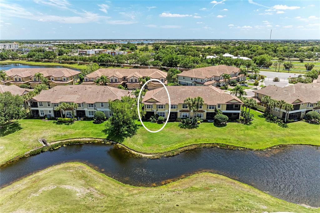An aerial view shows a multi-story residential building with a tiled roof near a pond — 8432 MIRAMAR WAY, LAKEWOOD RANCH, FL