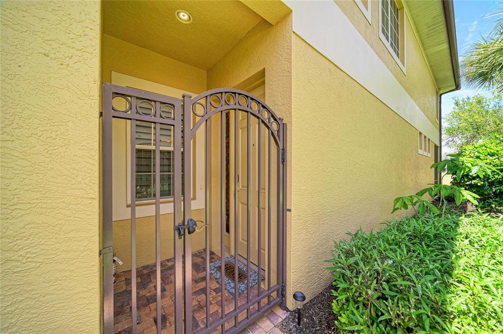 A metal gate leads to the front entryway of a yellow stucco house — 8432 MIRAMAR WAY, LAKEWOOD RANCH, FL