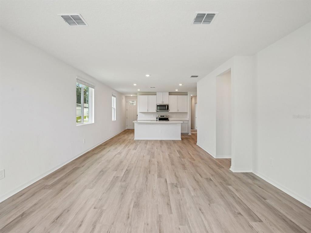An open-concept kitchen with white cabinets and an island overlooks a spacious living area — 1475 BREKEY WAY, ZEPHYRHILLS, FL