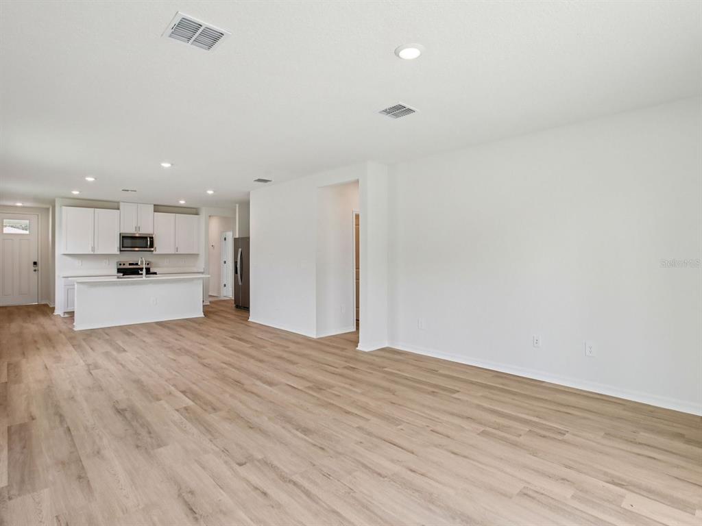 An open-concept living area features light wood-look flooring and a kitchen with white cabinetry — 1475 BREKEY WAY, ZEPHYRHILLS, FL