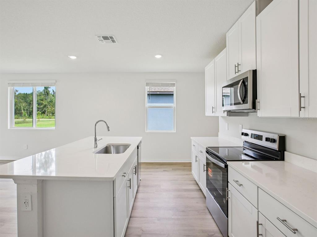 A modern kitchen features white cabinets, stainless steel appliances, and a large central island — 1475 BREKEY WAY, ZEPHYRHILLS, FL