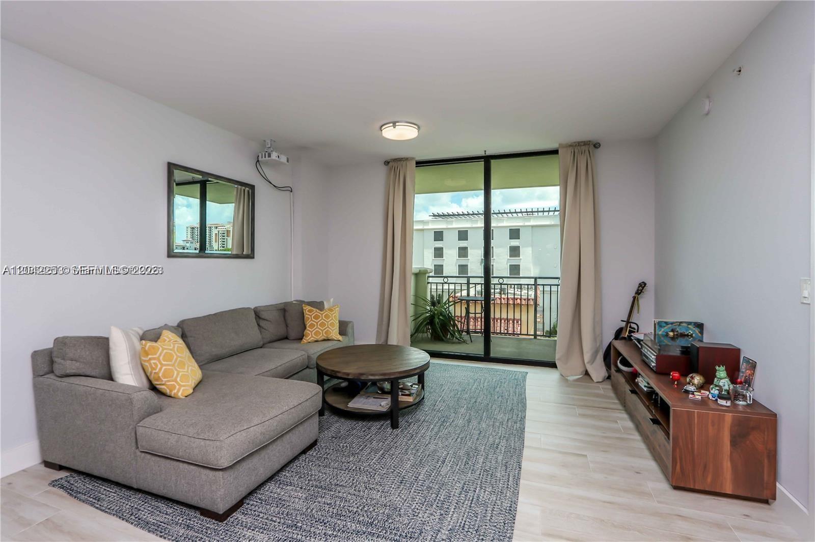 A living room features a gray sectional sofa, a round coffee table, and a balcony — 1300 Ponce De Leon Blvd # 500, Coral Gables FL 33134, CORAL GABLES, FL