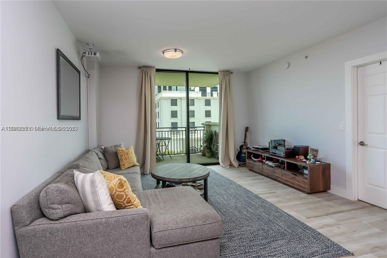 A living room features a gray sectional sofa, a round coffee table, and a balcony — 1300 Ponce De Leon Blvd # 500, Coral Gables FL 33134, CORAL GABLES, FL