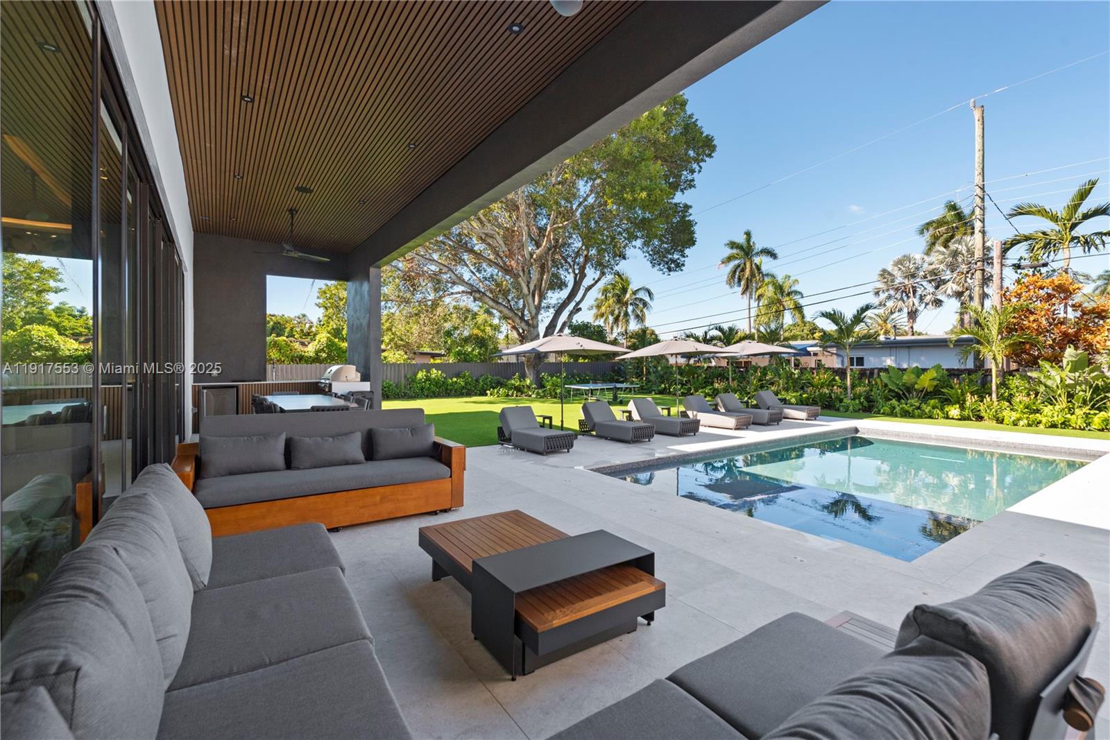 A covered patio features outdoor seating, a coffee table, and a pool overlooking a yard — 1881 NE 196th Ter, Miami FL 33179, MIAMI, FL