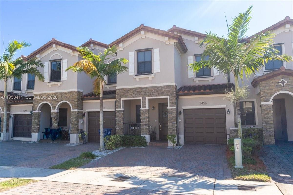 A two-story townhouse features a stone facade, a brown garage door, and palm trees — 11456 SW 252nd Ter, Homestead FL 33032, HOMESTEAD, FL