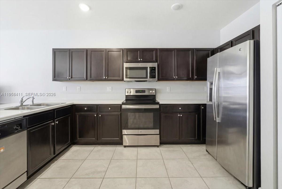 A kitchen features dark wood cabinets, stainless steel appliances, white countertops, and light tile flooring — 11456 SW 252nd Ter, Homestead FL 33032, HOMESTEAD, FL