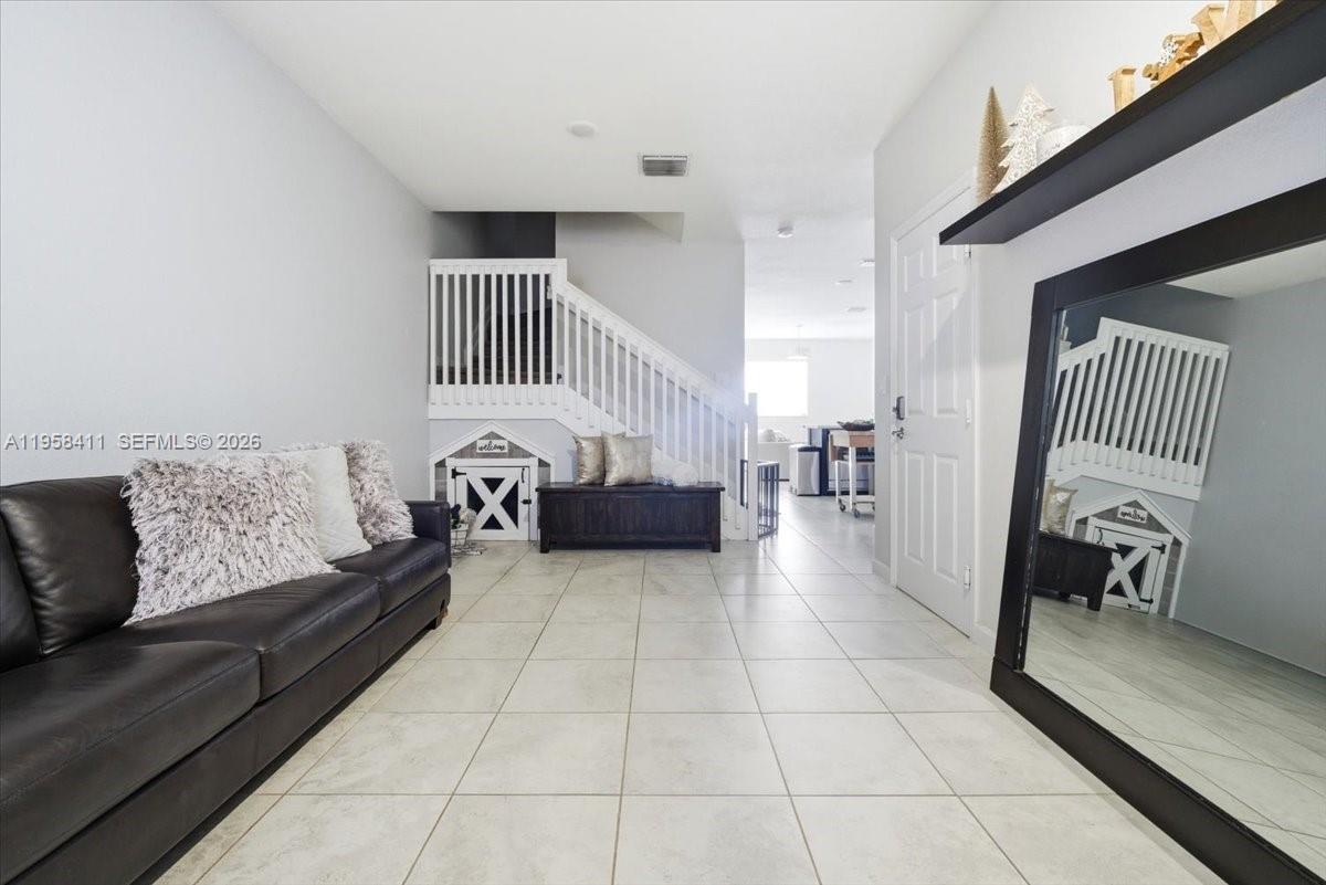 A living room features a dark leather sofa, tile flooring, and a large wall mirror — 11456 SW 252nd Ter, Homestead FL 33032, HOMESTEAD, FL