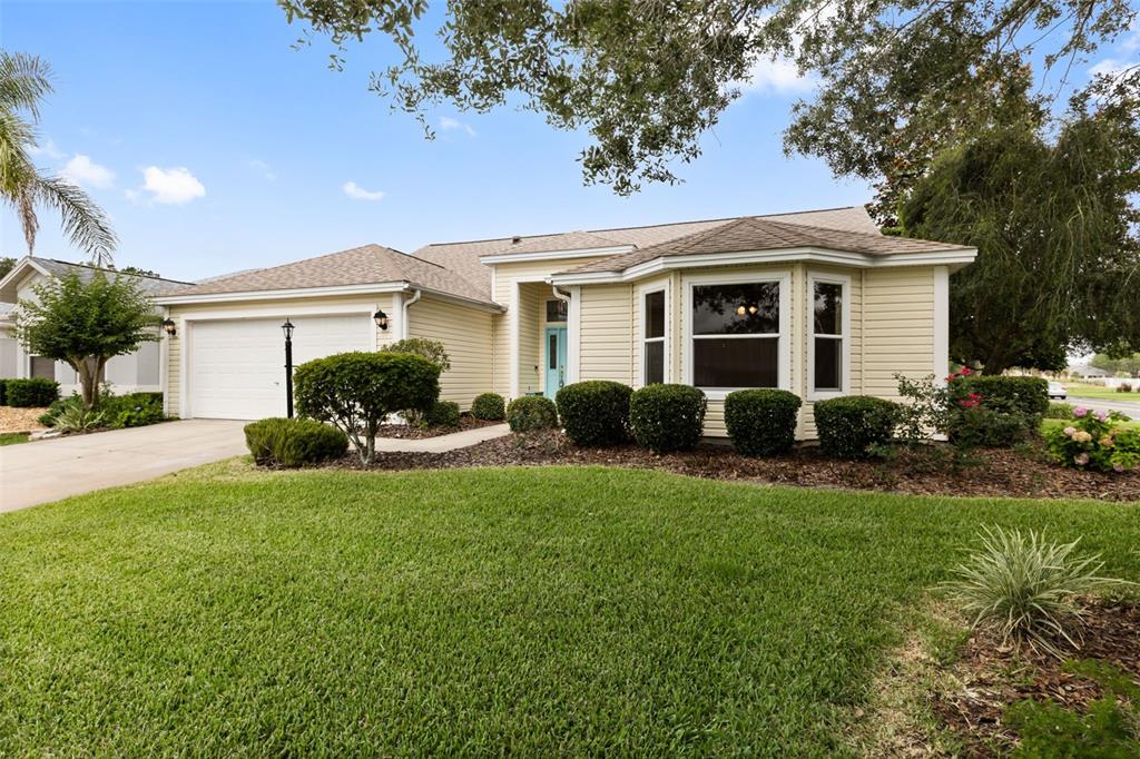 A single-story house with light yellow siding, a two-car garage, and a front lawn — 1312 BAEZ WAY, THE VILLAGES, FL