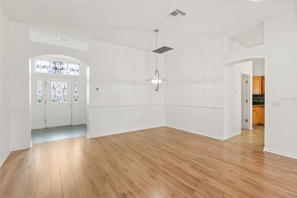 An empty dining room with light wood floors, white walls, and a modern chandelier — 1312 BAEZ WAY, THE VILLAGES, FL
