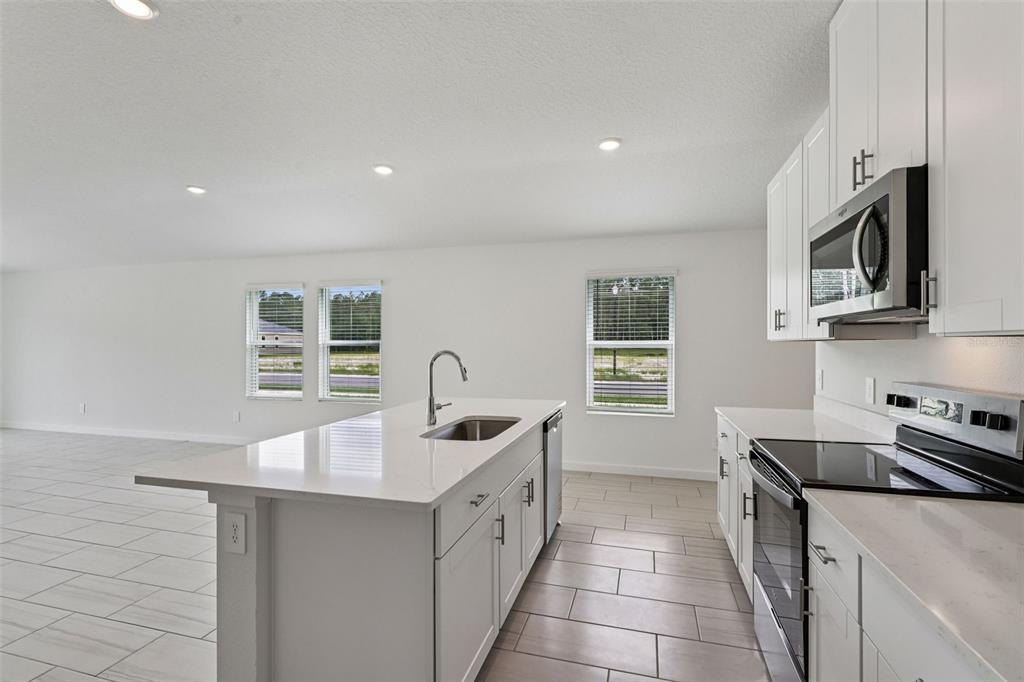 A modern kitchen features white cabinetry, a quartz island with a sink, and tiled flooring — 100 WANDERING CREEK WAY, PALM COAST, FL