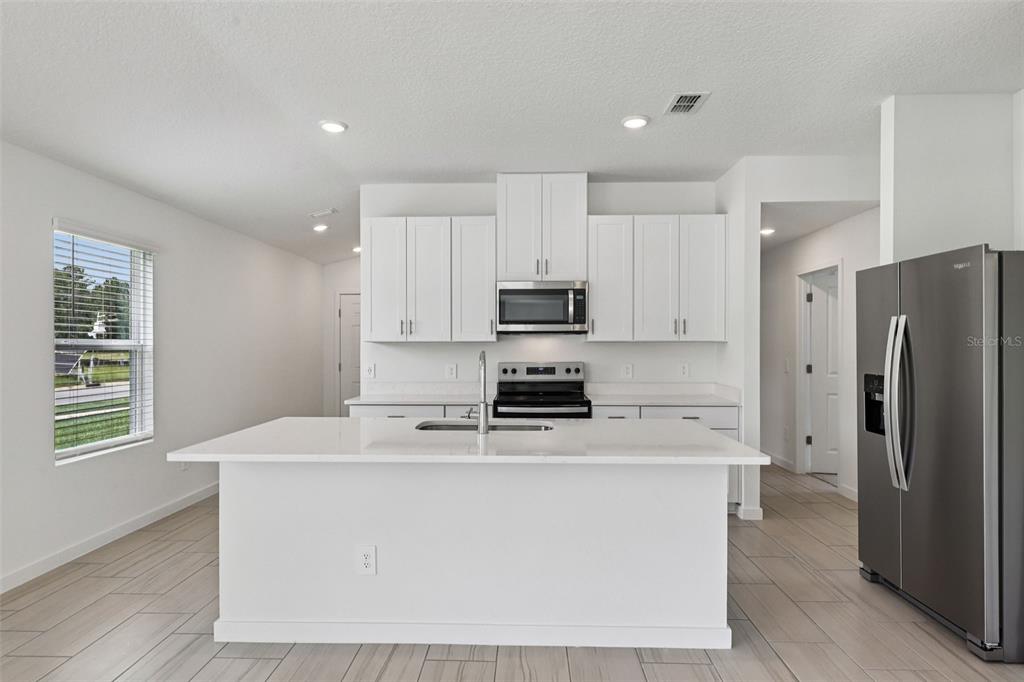 A modern kitchen features white cabinets, a central island with a sink, and stainless appliances — 100 WANDERING CREEK WAY, PALM COAST, FL