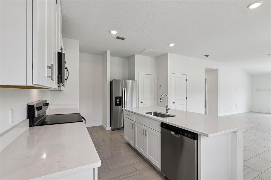 A modern kitchen features white cabinets, stainless steel appliances, and a large quartz island — 100 WANDERING CREEK WAY, PALM COAST, FL