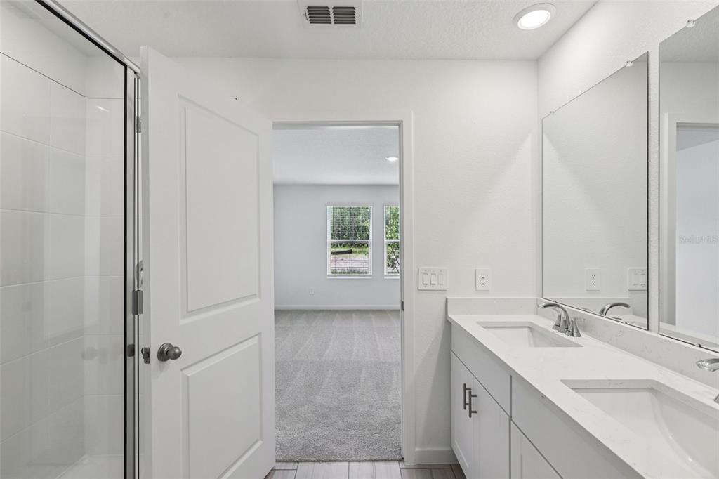 A bathroom with a glass shower, double vanity, and an open doorway to a bedroom — 100 WANDERING CREEK WAY, PALM COAST, FL