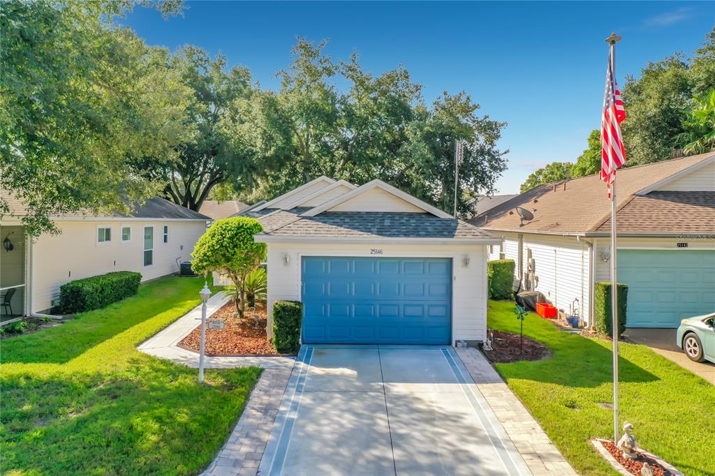 A single-story house with a blue garage door, a paved driveway, and an American flag — 25146 CRANES ROOST CIRCLE, LEESBURG, FL