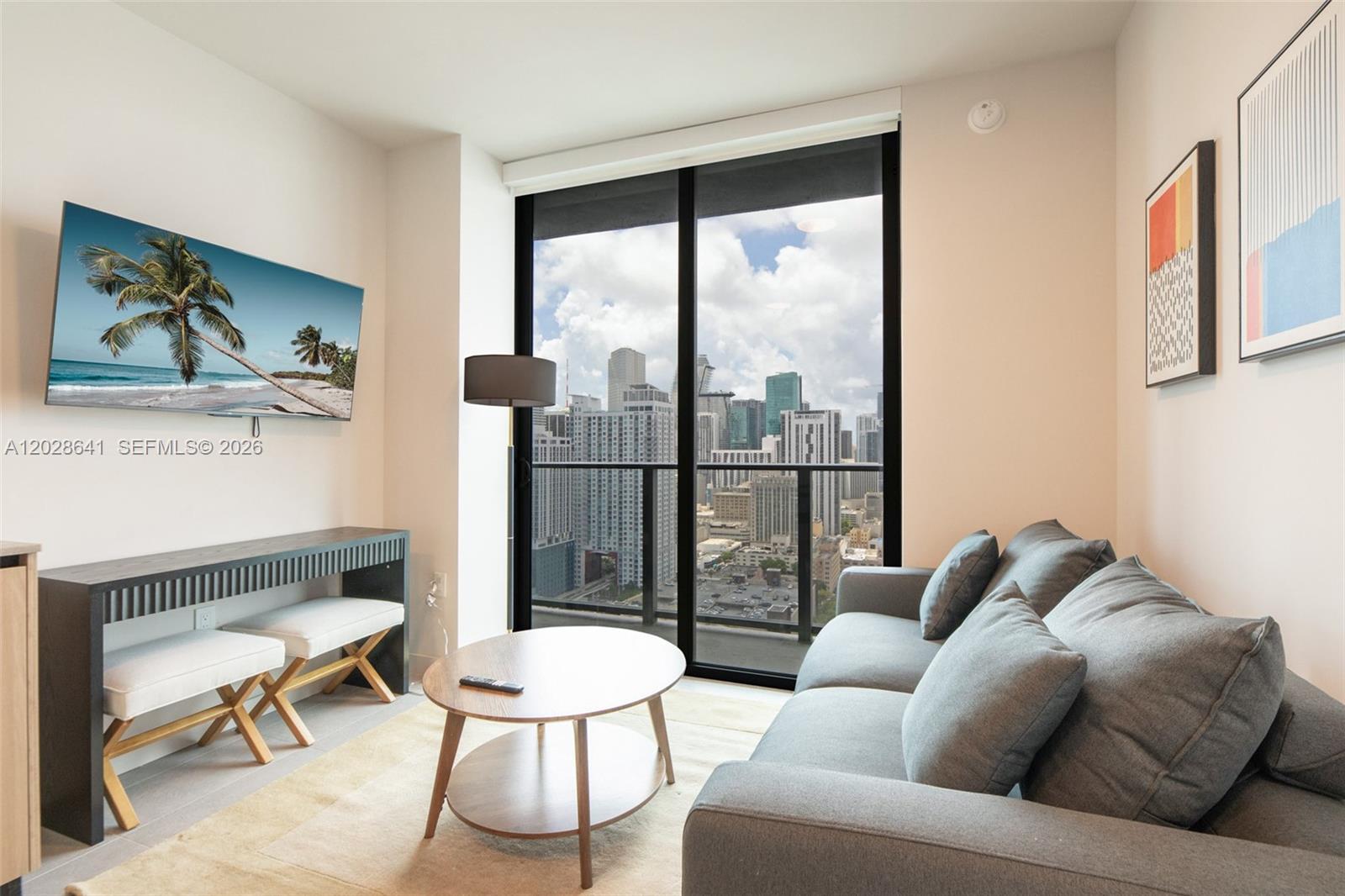 A modern living room features a gray sofa, coffee table, and a balcony with city views — 121 NE 5th St # 3103, Miami FL 33132, MIAMI, FL