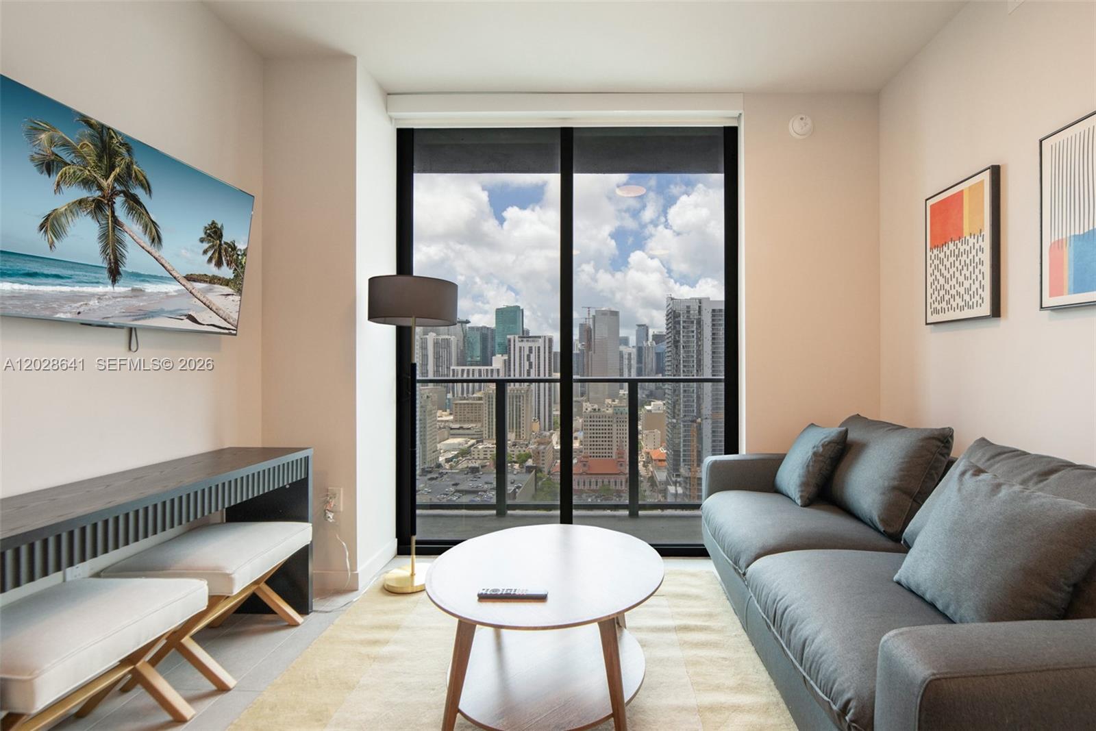 A living room features a grey sofa, a coffee table, and a view of city skyscrapers — 121 NE 5th St # 3103, Miami FL 33132, MIAMI, FL