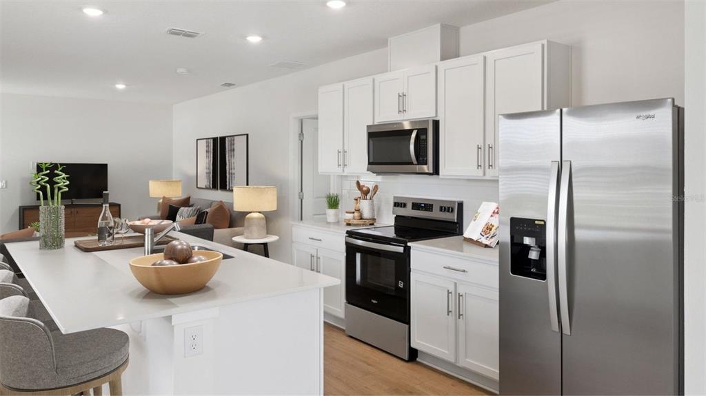 A modern kitchen with white cabinets, stainless steel appliances, and a large island with seating — 5144 BLANKET FLOWER STREET, APOPKA, FL