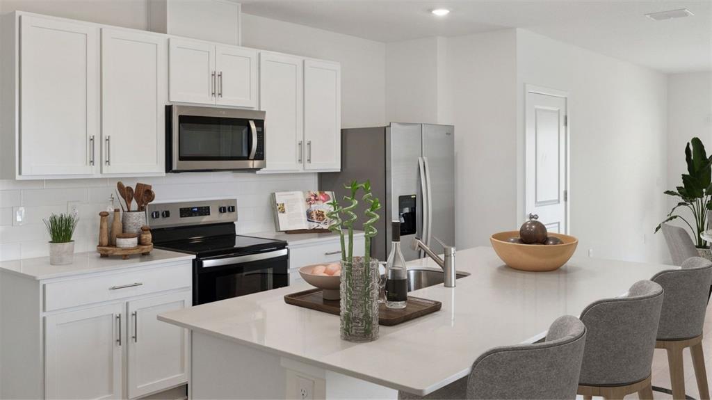 A modern kitchen features white cabinets, stainless steel appliances, and a large central island — 5144 BLANKET FLOWER STREET, APOPKA, FL