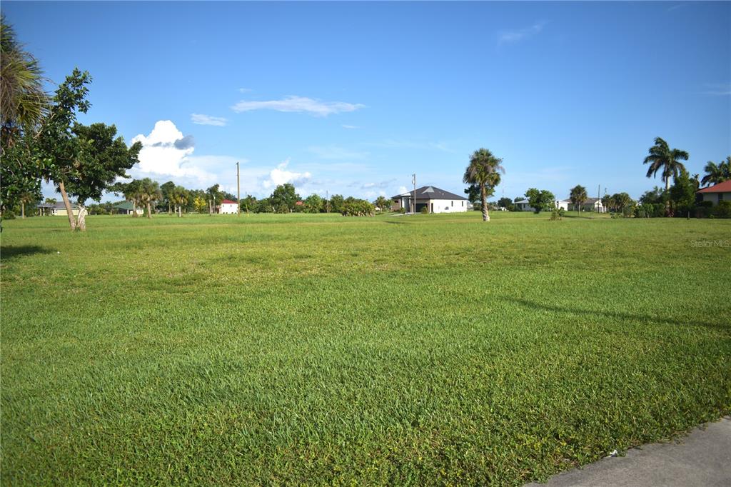 A wide, grassy vacant lot is surrounded by scattered trees and nearby residential houses — 16298 CAPE HORN BOULEVARD, PUNTA GORDA, FL