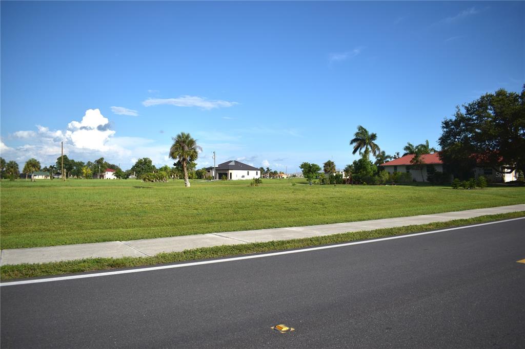 A paved road runs alongside a grassy vacant lot with a sidewalk and distant houses — 16298 CAPE HORN BOULEVARD, PUNTA GORDA, FL