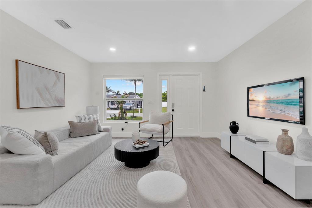 A bright living room features a gray sofa, a round coffee table, and a wall-mounted television — 1115 Stillwater Drive, Jupiter FL 33458, JUPITER, FL